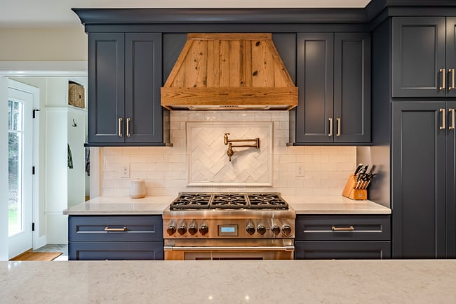 dark blue cabinets with wood finished vent above metal stove