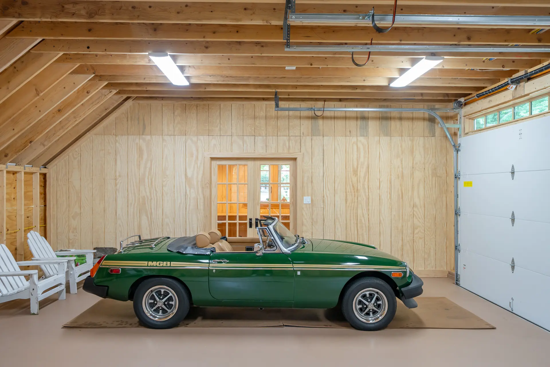 Interior of a two-car garage bay with exposed wood rafters and a green vintage MGB convertible