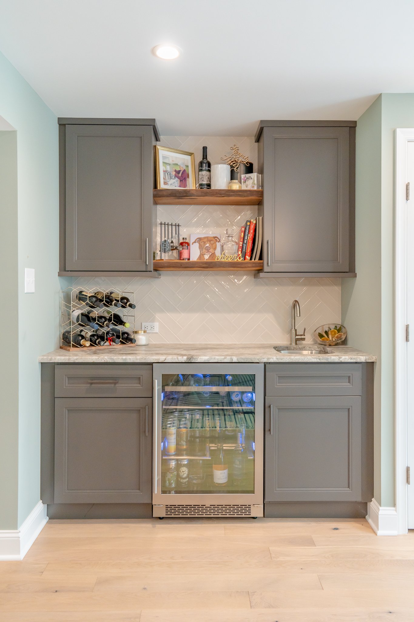 a wet bar featuring soft gray cabinets, floating shelves, a sink, and a beverage refrigerator