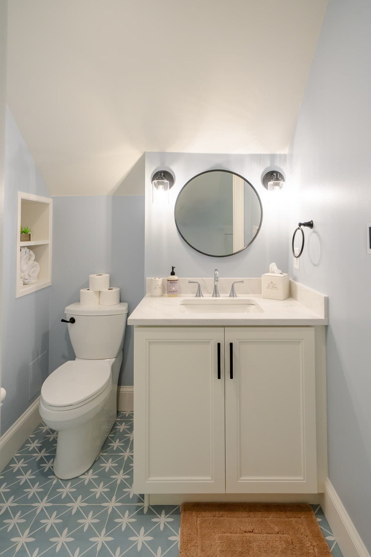 Tiny bathroom with a toilet and wood vanity. A single round-edge mirror on the wall
